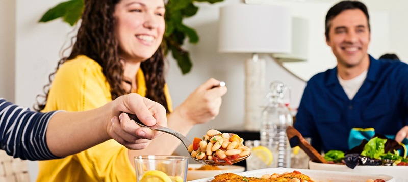 A heaping spoonful of beans in front of people at a dinner table