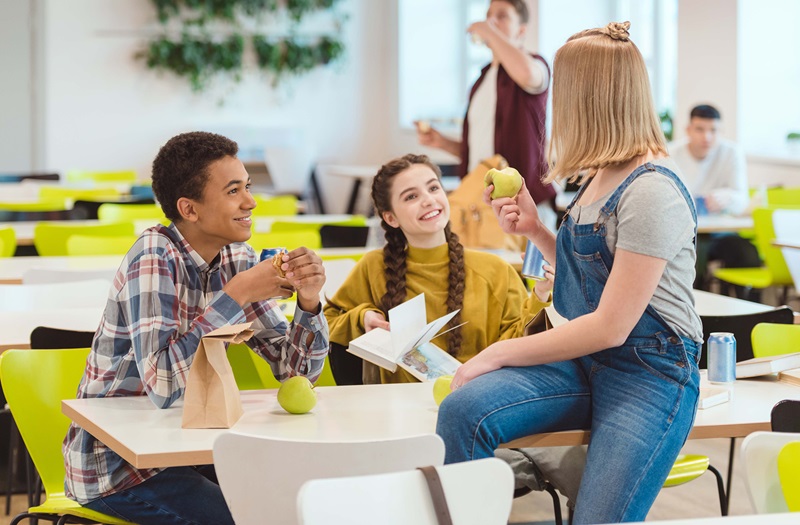 Kids sitting in a cafeteria smiling and talking
