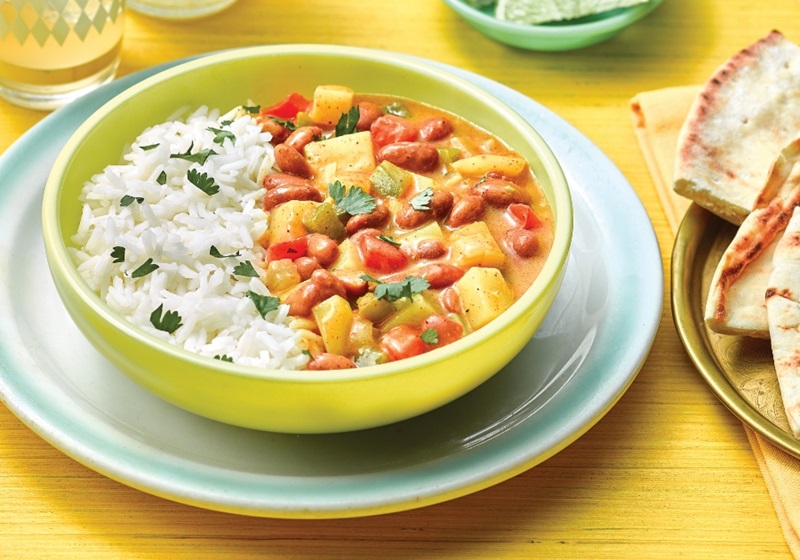 Rice and beans topped with cilantro, in a yellow bowl, served with pita wedges