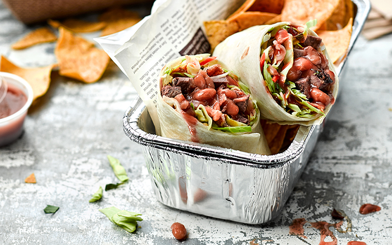 Foil tray with a baked bean burrito cut in half in front of tortilla chips