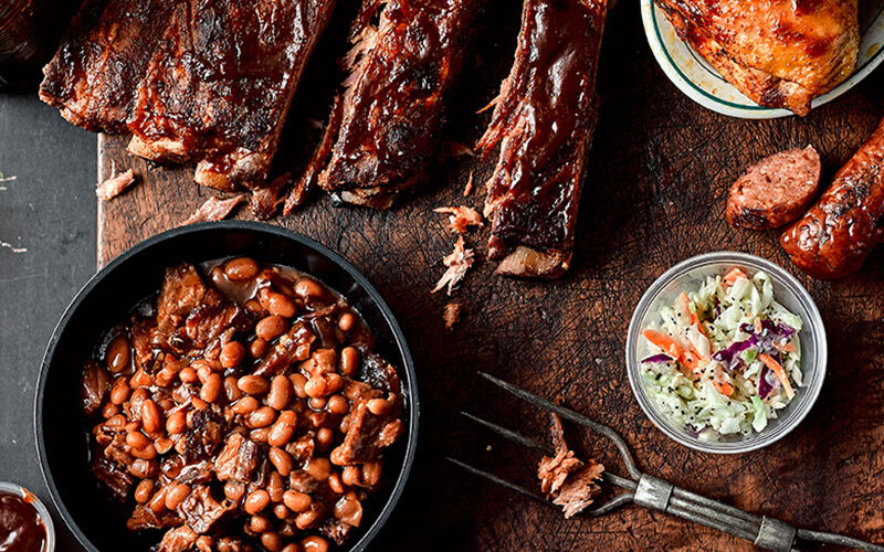 Bush’s Best® Bean Pot Baked Beans simmered with brisket and BBQ sauce sits on the side of the Big Rig BBQ Plate entree for a flavor-packed restaurant, healthcare or C&U foodservice recipe.