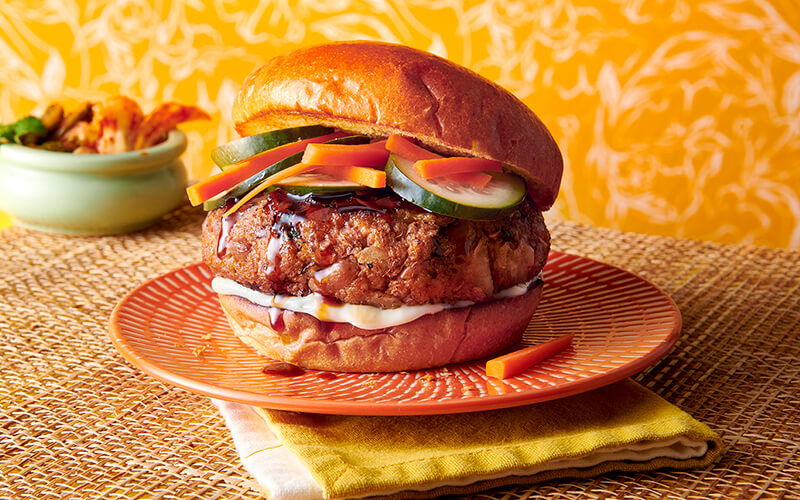 Toasted Korean BBQ Bean Burger is placed on an orange plate with white decals.
