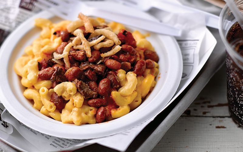 Bowl of mac n cheese topped with steak chili and onion strings