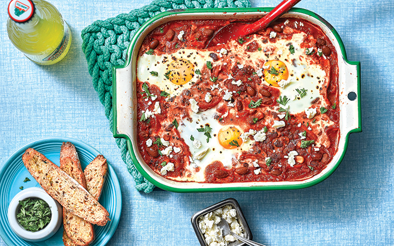 Shakshuka Dip served in a green and cream oven-safe pan and topped with freshly chopped parsley and over easy eggs. 