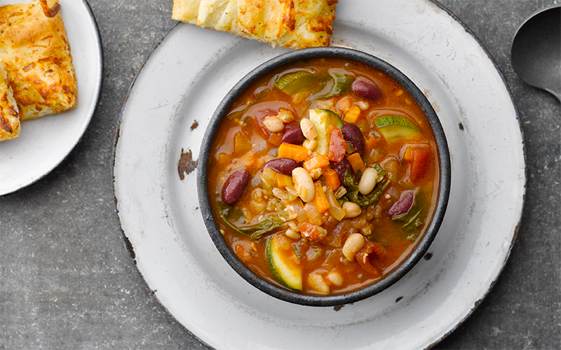 Pasta e fagioli soup in a bowl with some garlic breadsticks on a plate