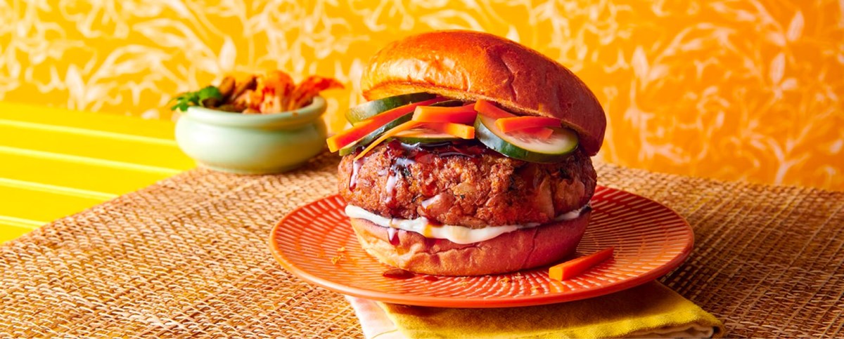 Fresh bean burger topped with veggies on an orange plate