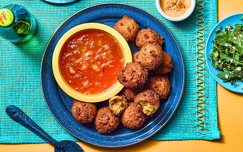 Blue plate piled with hush puppies around a yellow bowl of mango chutney