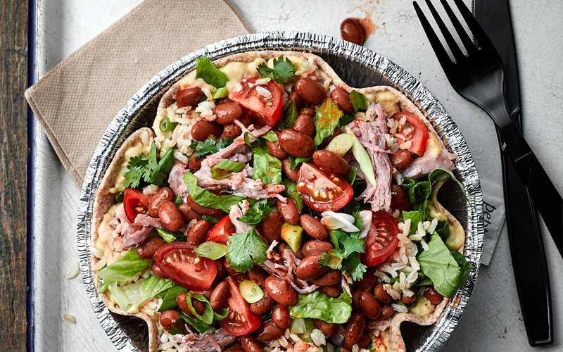 Foil salad bowl lined with a tortilla filled with hummus, rice, Bush's Easy Entrees Texas Ranchero Pinto Beans, pulled pork, and tomatoes.