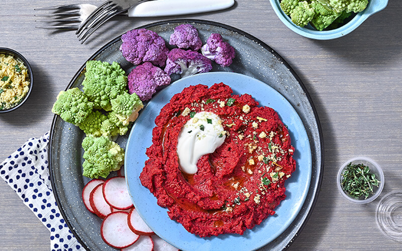 Roasted Beet Hummus topped with sour cream. Served next to the hummus are Belgium endives, baby red radishes and sliced Italian bread. 