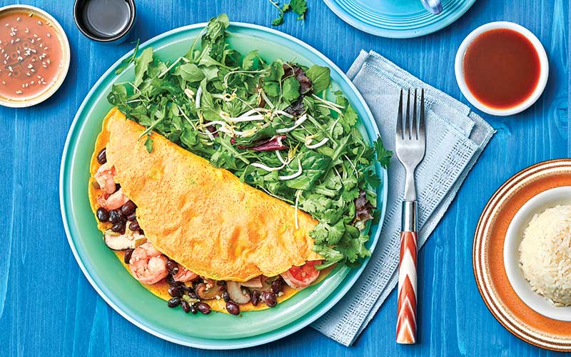 A Scallion Pancake folded around a mixture of black beans, shrimp, and mushrooms served next to a stack of greens.