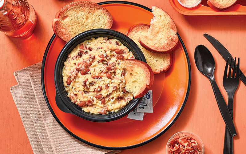 Polenta Dip served with toasted baguettes on an orange plate and a side of parmesan cheese. 